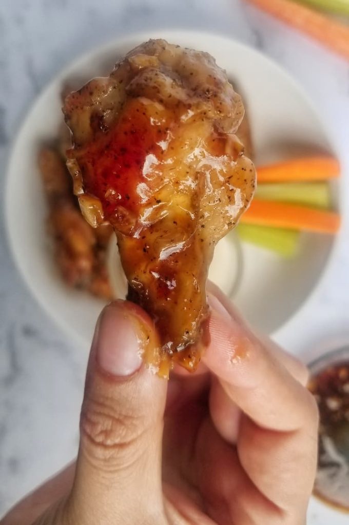 hand holding up a saucy wing to the camera with celery and carrots in the background