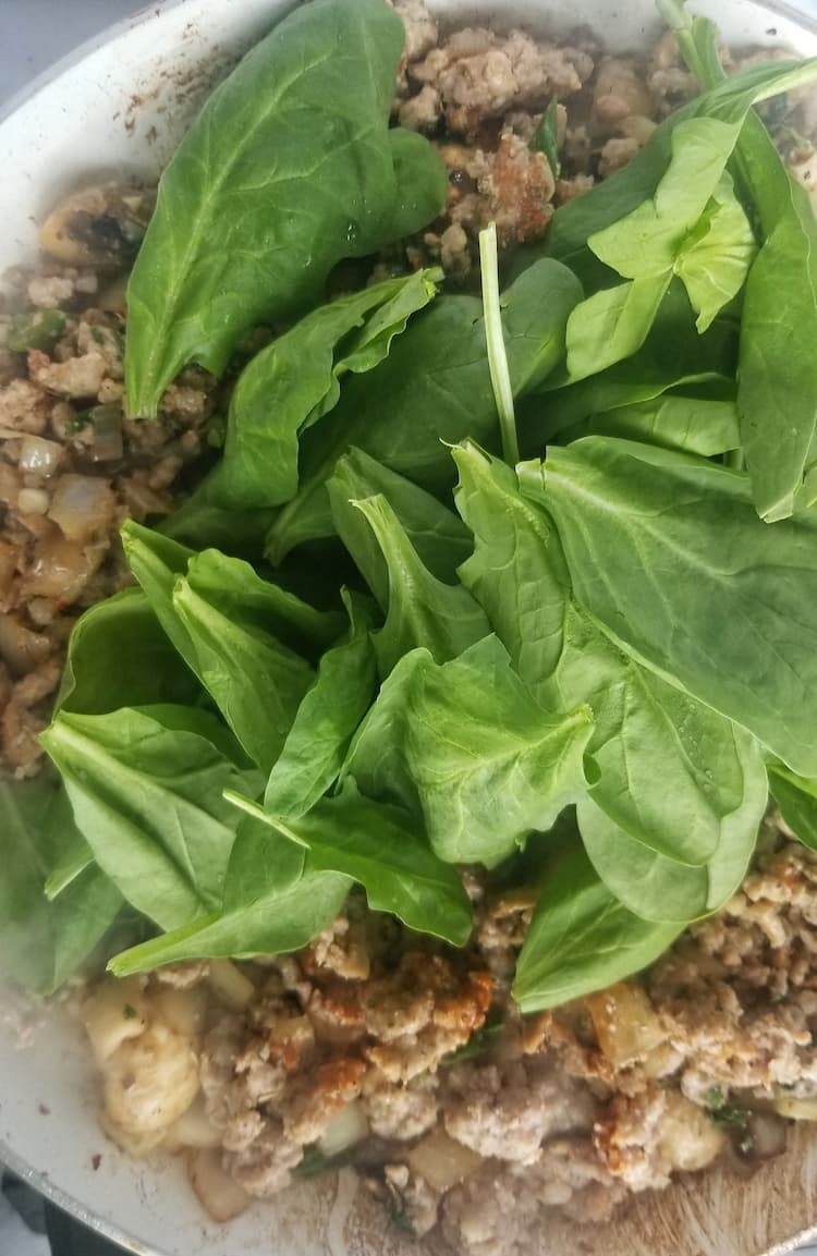 skillet with browned ground meat and fresh spinach