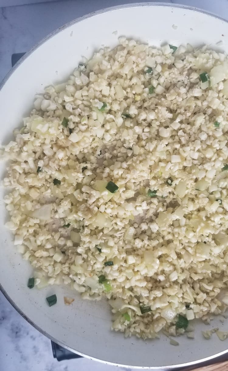 skillet with riced cauliflower, lime zest and chopped cilantro, chopped white onions