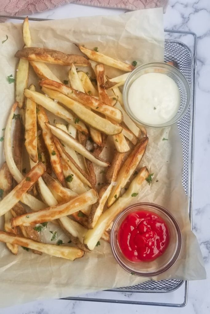 tray of air fryer fries topped with parsley with bowl of ketchup and white dip