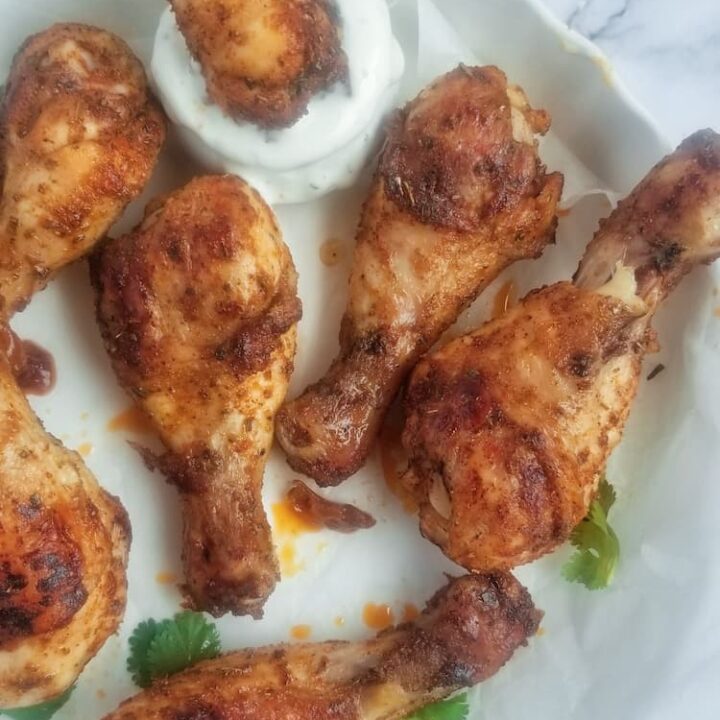 7 baked chicken drumsticks on a white circular dish, one of the drumsticks is in a creamy white dipping sauce, garnished with fresh parsley