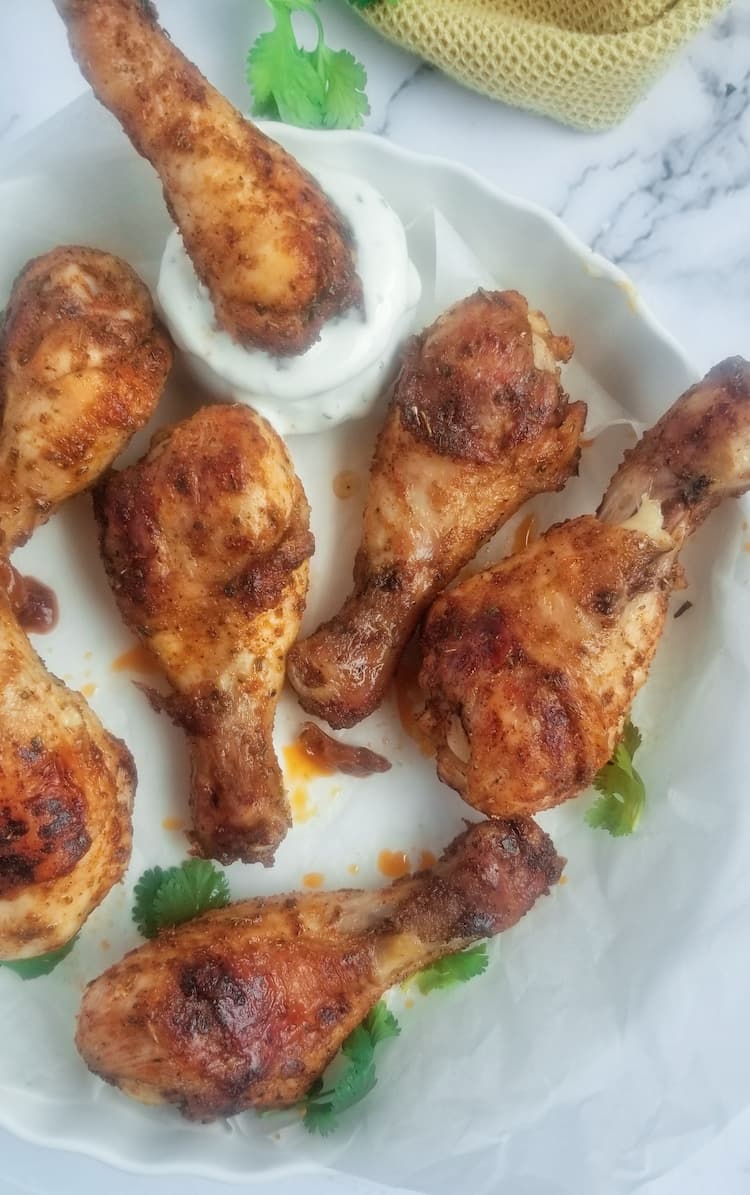 7 baked chicken drumsticks on a white circular dish, one of the drumsticks is in a creamy white dipping sauce, garnished with fresh parsley