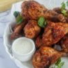 baked chicken drumsticks in a circular dish garnished with fresh parsley, creamy white sauce on the side