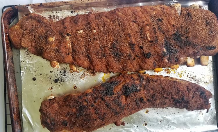 Two cooked racks of ribs on a foil lined baking sheet