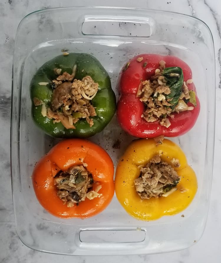 casserole dish with 4 stuffed peppers, 1 green, 1 yellow, 1 red, 1 orange, stuffed with spinach and ground meat