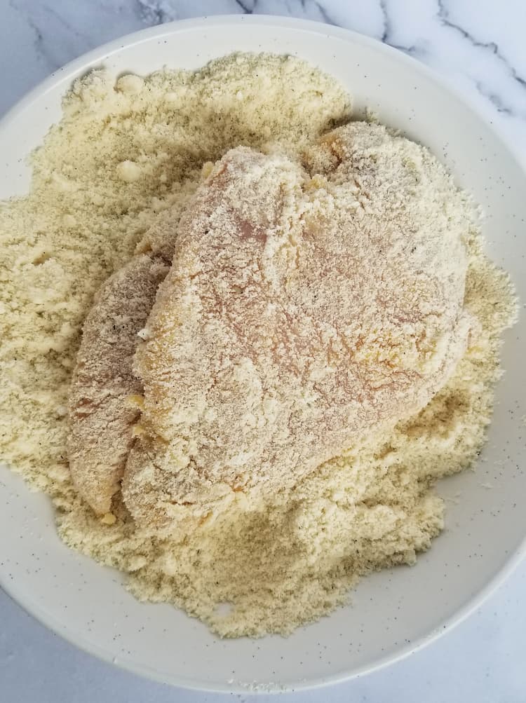 plate of flour and parmesan cheese mixture with a coated chicken breast in the middle
