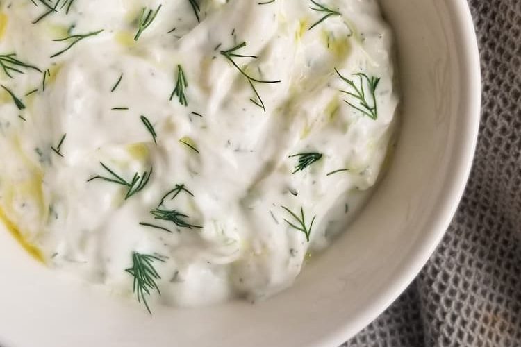 bowl of homemade tzatziki sauce with fresh dill and olive oil on top