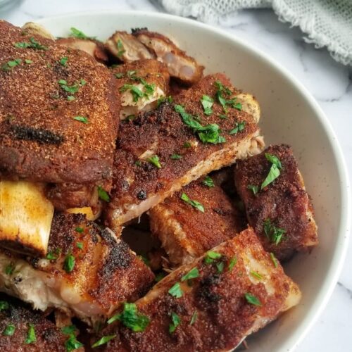 bowl of cooked pork ribs topped with fresh chopped parsley