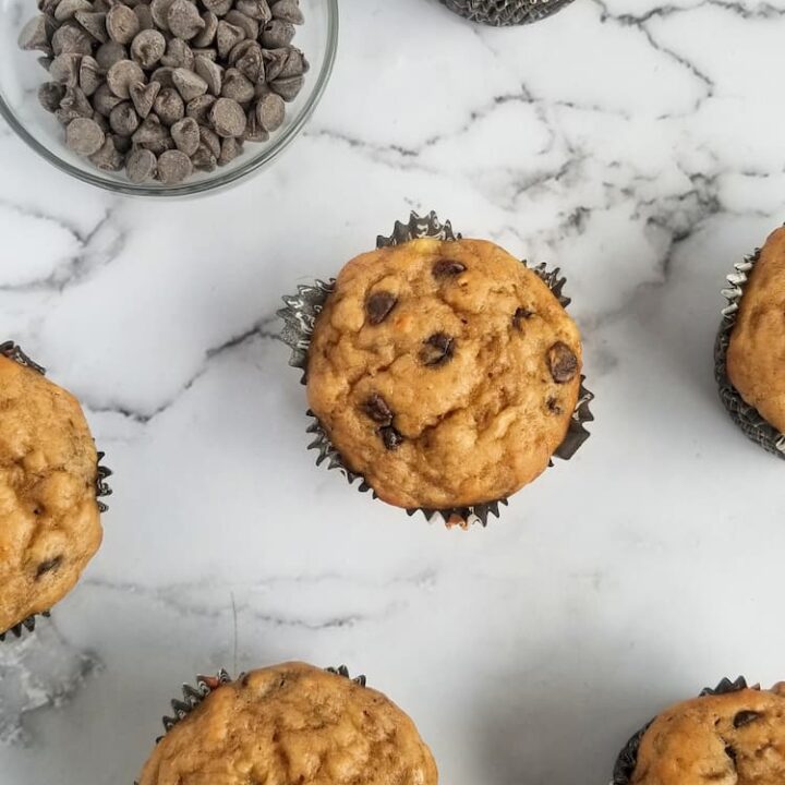 small bowl of chocolate chips next to 6 freshly baked chocolate chip muffins