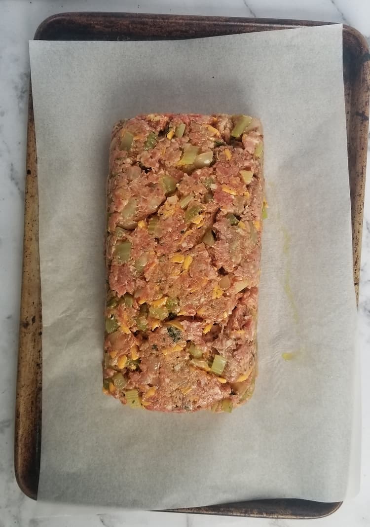 sheet pan with parchment paper with an uncooked meatloaf