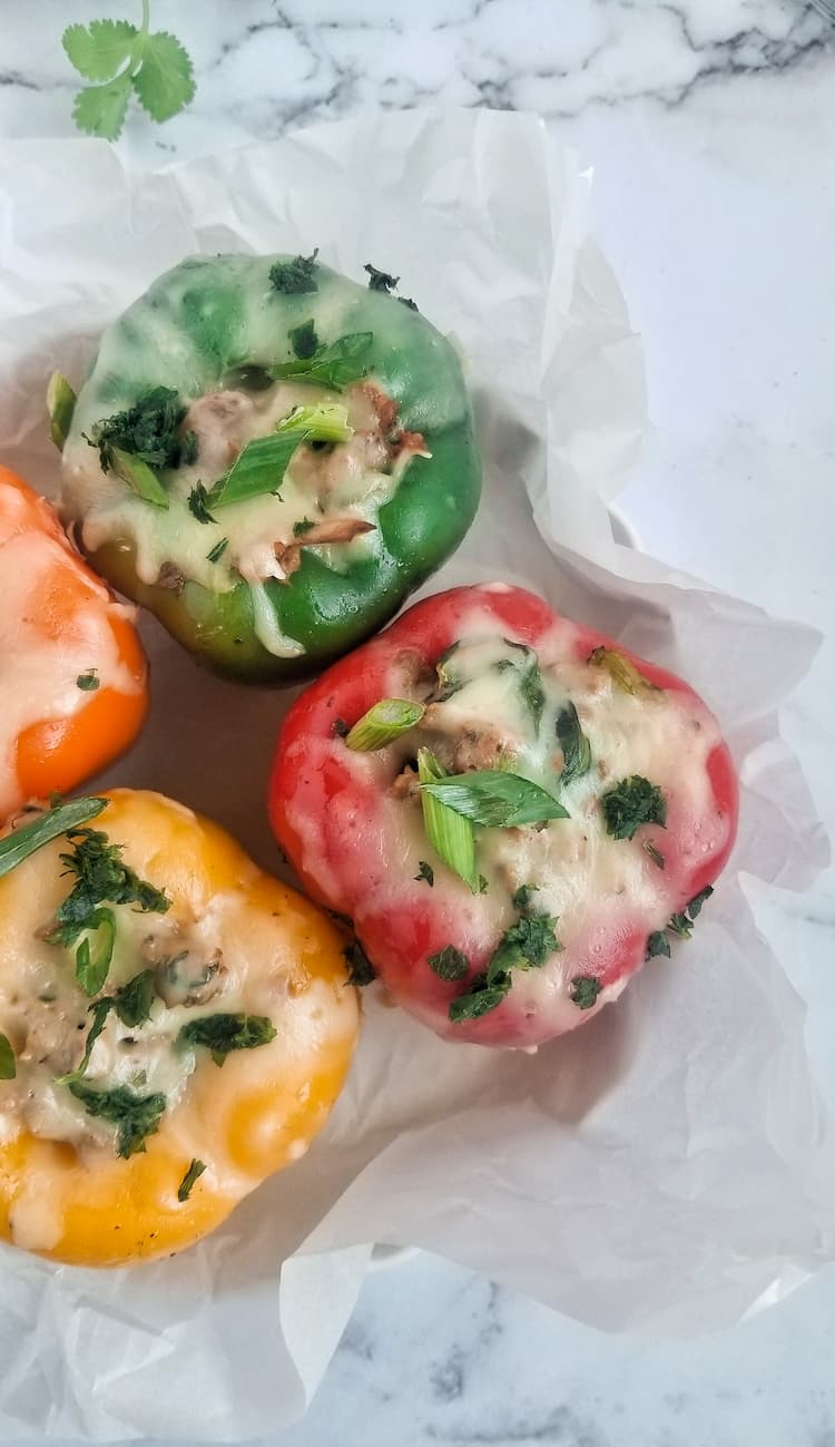 4 bell peppers, 1 green, 1 red, 1 orange and 1 yellow in a casserole dish, fresh melted mozzarella cheese on top with fresh parsley and chopped green onions, spinach and ground meat in the peppers