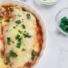 chicken breast topped with melted mozzarella cheese, tomato sauce and fresh parsley. Bowl of chopped fresh parsley and grated parmesan cheese in the background