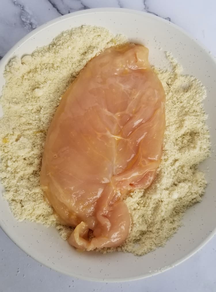 plate of flour and parmesan cheese mixture with a raw chicken breast in the middle