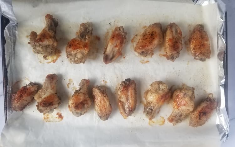 parchment lined baking sheet with half cooked chicken wings spread out in a single layer