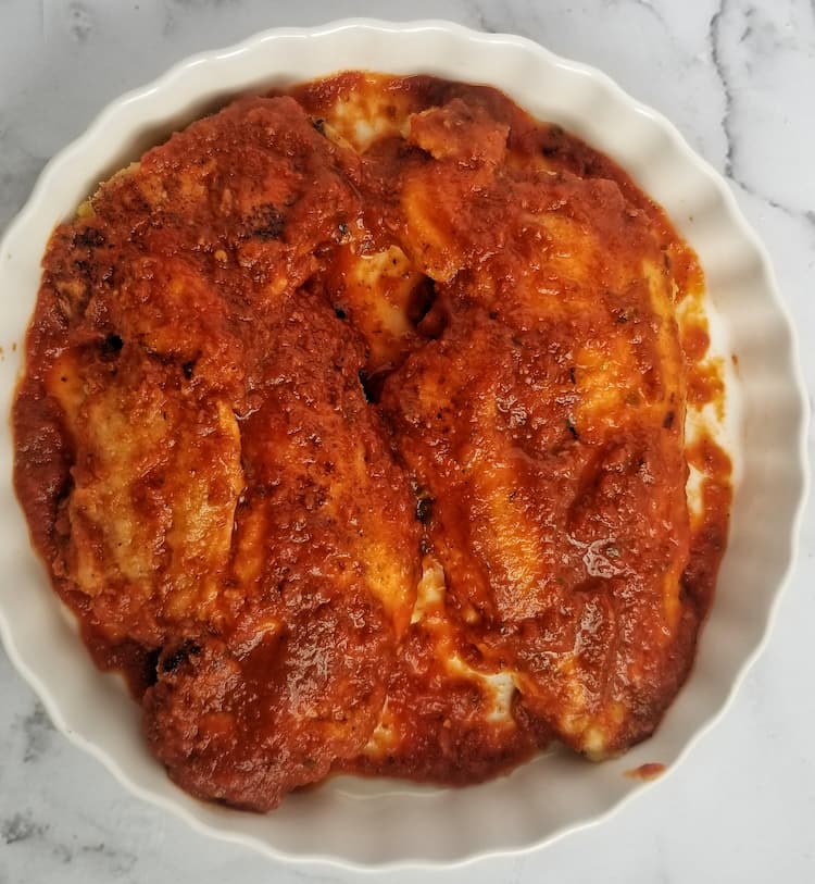 two chicken breasts in a white dish covered in tomato sauce