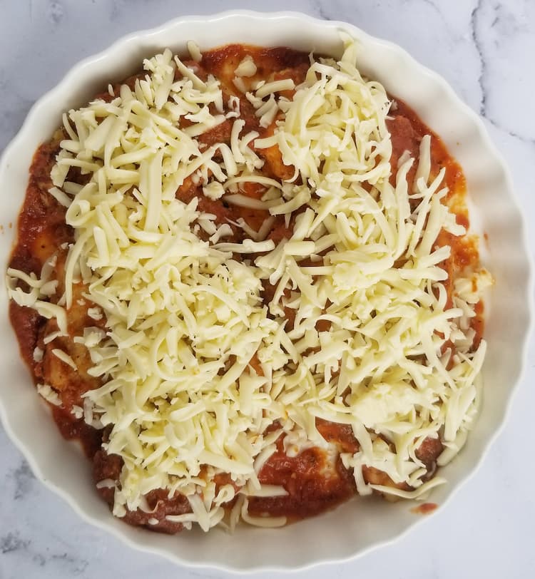white dish with two chicken breasts covered in tomato sauce and shredded mozzarella cheese