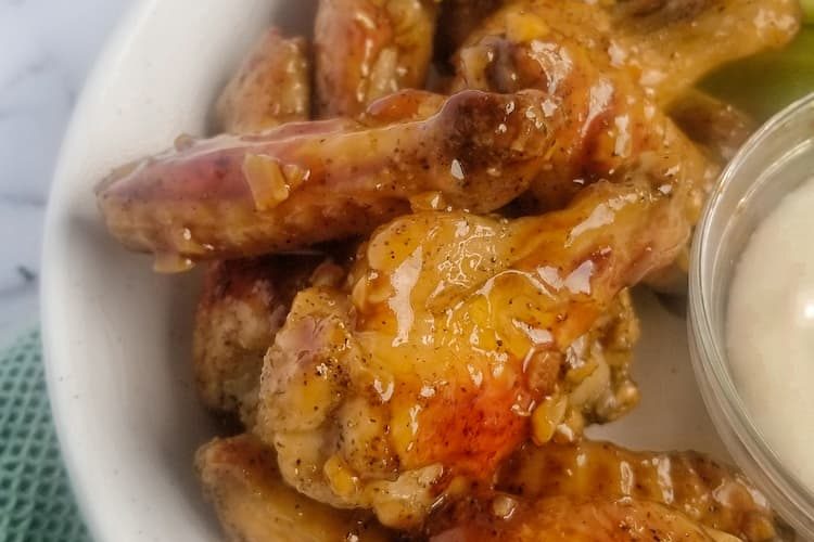 side view of bowl of honey garlic chicken wings with homemade honey garlic sauce in a bowl with a rubber spatula in the background