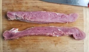 cutting board with two long pieces of pork tenderloin