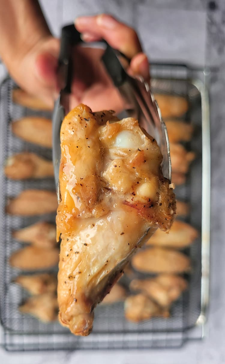 hand holding up tongs to the camera with a cooked chicken drumstick