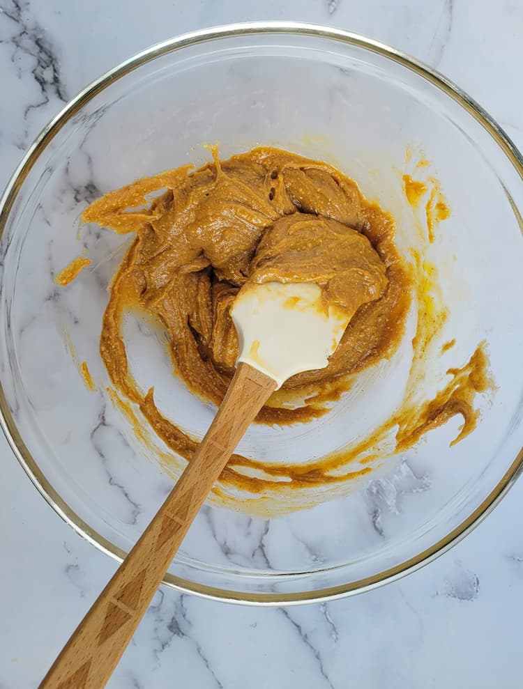 bowl of creamy peanut butter batter for cookies with a rubber spatula in bowl