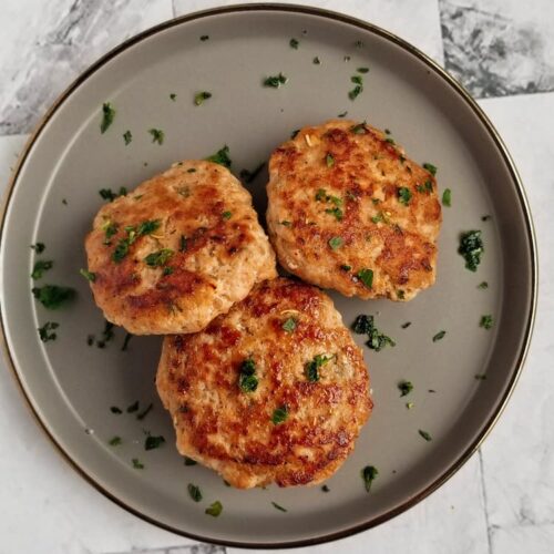 3 breakfast sausage patties on a plate with fresh chopped parsley