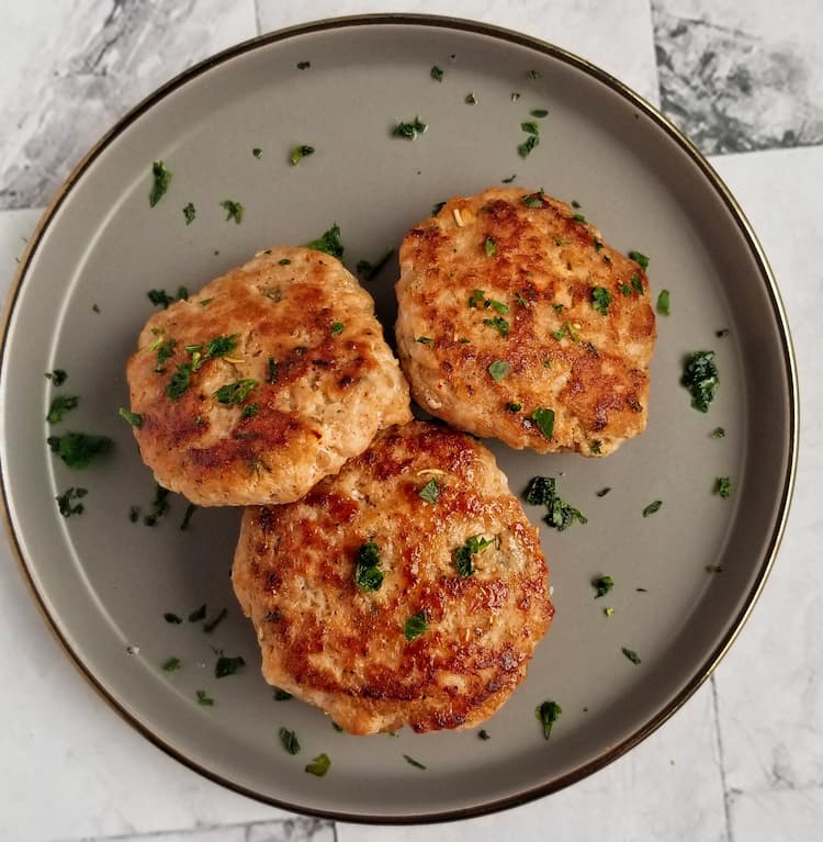3 breakfast sausage patties on a plate with fresh chopped parsley
