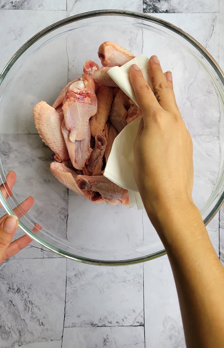 raw chicken wings in a glass bowl, hand patting them down with paper towel