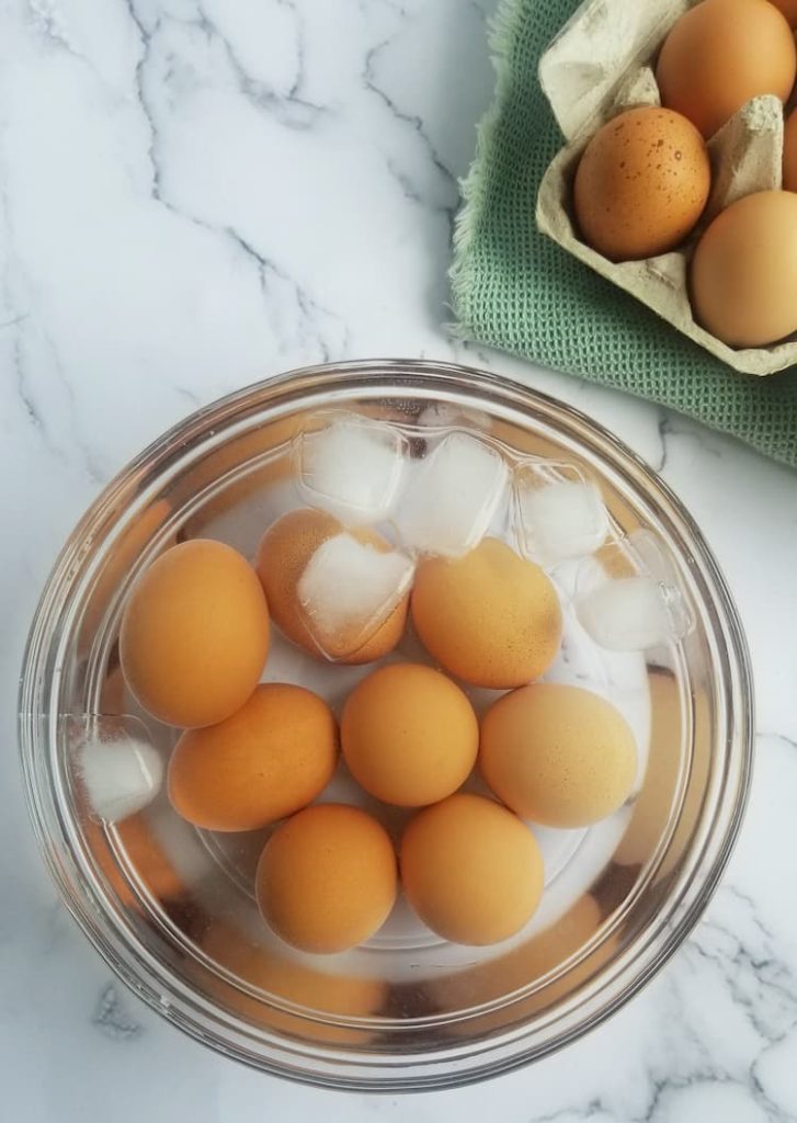 whole brown eggs in a bowl of ice water next to a carton of brown eggs