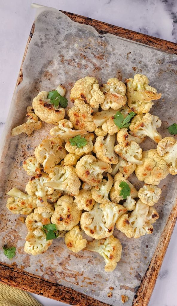 roasted cauliflower on a parchment lined baking sheet topped with chopped parsley