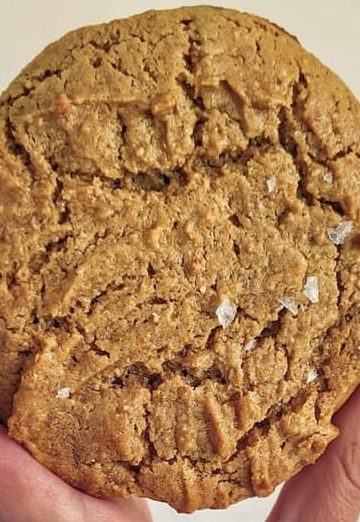 hand holding up a giant flourless peanut butter cookie with flaky salt