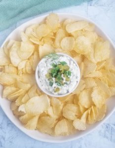 bowl of dill pickle dip topped with green onions and chopped pickles with some chips around it