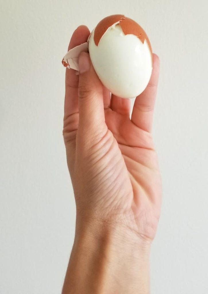 hand holding up a half peeled hard boiled egg made in the instant pot