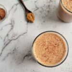 chocolate peanut butter smoothie with another one in the background, spoonful of peanut butter in the background, ramekin of cocoa on the side