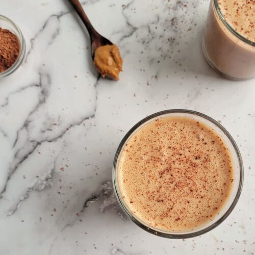 chocolate peanut butter smoothie with another one in the background, spoonful of peanut butter in the background, ramekin of cocoa on the side