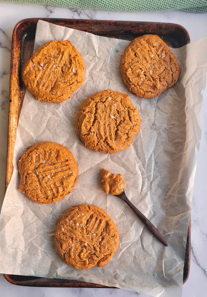5 peanut butter cookies (flourless) on a parchment lined baking sheet with a spoonful of peanut butter
