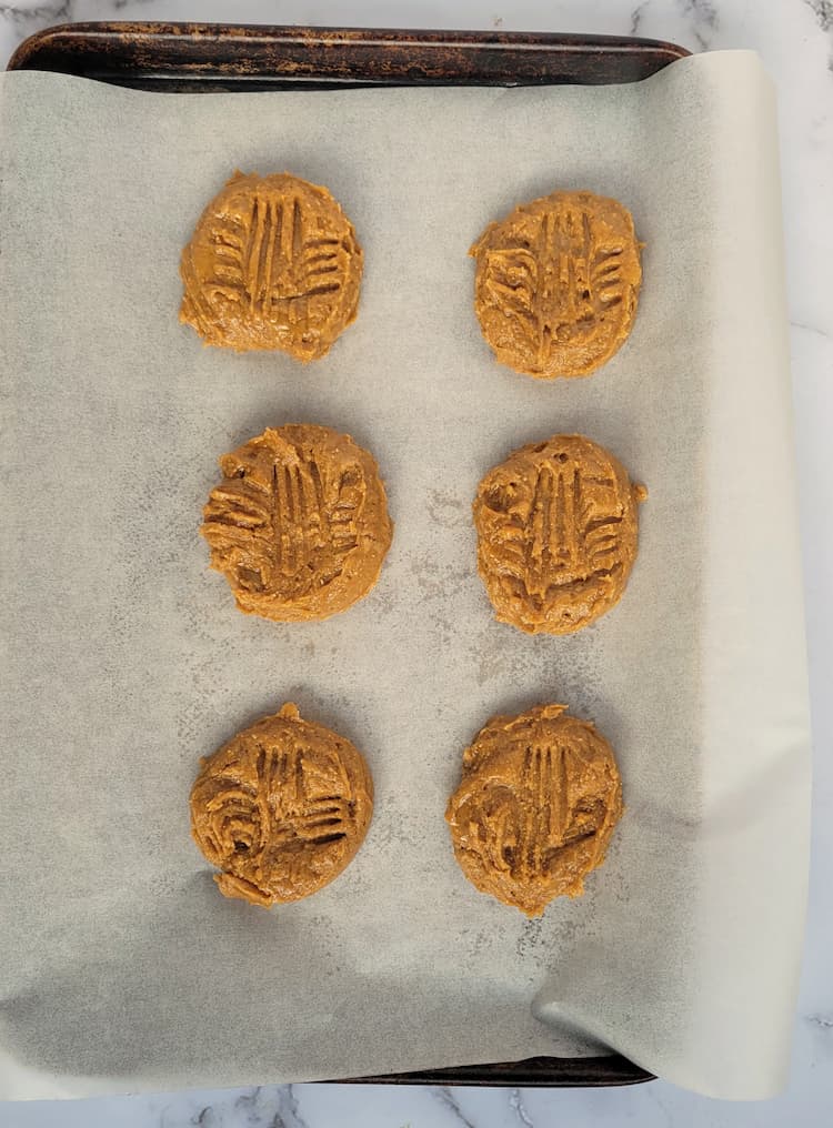 parchment lined baking sheet with 6 flattened flourless peanut butter cookies before baking