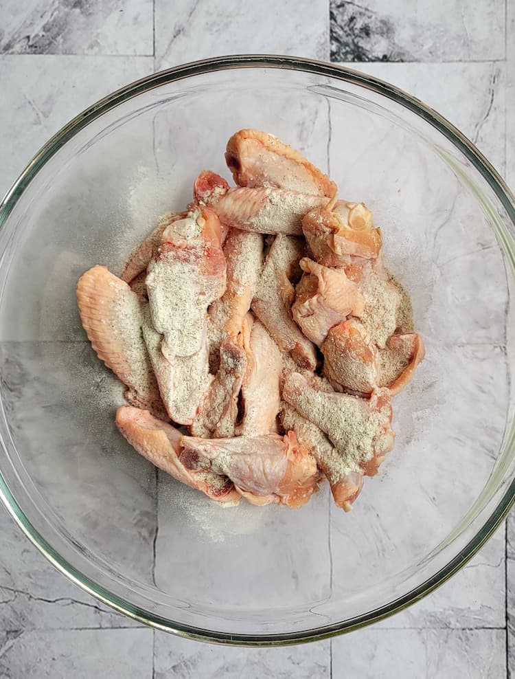 raw chicken wings in a glass bowl with some seasonings
