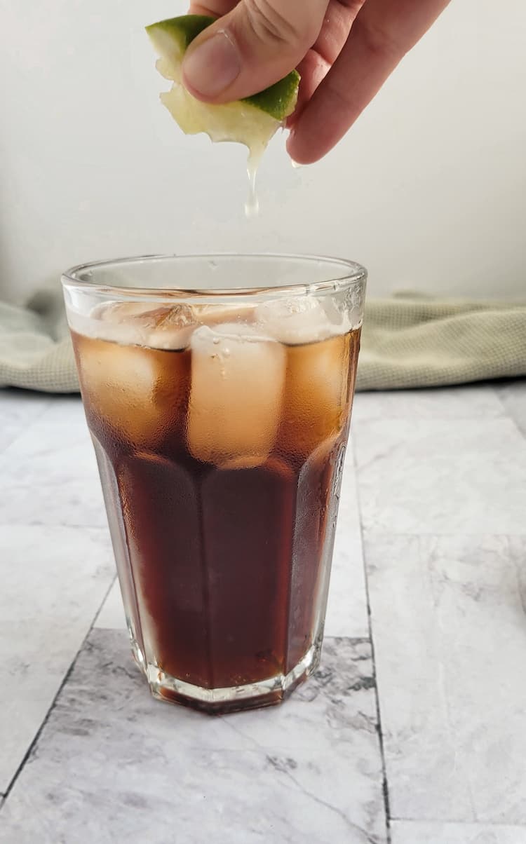 hand squeezing a fresh lime wedge into a glass of rum and coke with ice