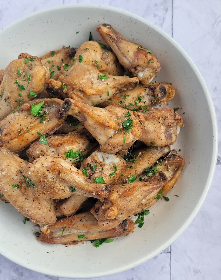 bowl of air fried chicken wings seasoned with salt, pepper and fresh chopped parsley