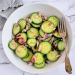 bowl of cucumber salad with dill with diced red onions, fork in the bowl