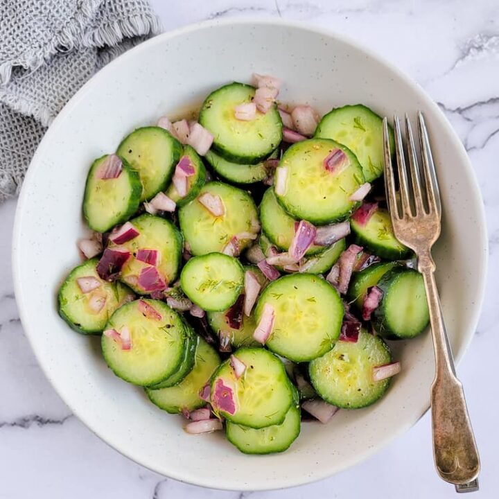 bowl of cucumber salad with dill with diced red onions, fork in the bowl
