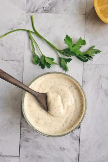 a bowl of homemade ranch dressing with a wooden spoon, half a lemon in the background with some parsley