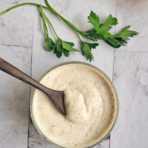 a bowl of homemade ranch dressing with a wooden spoon, half a lemon in the background with some parsley