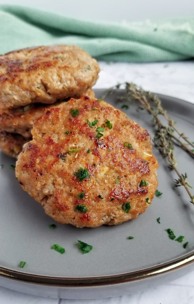 breakfast sausage patties on a plate with fresh chopped parsley and sprigs of fresh thyme