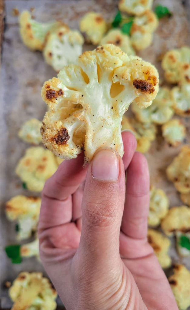 hand holding up a piece of roasted cauliflower over a tray of the rest