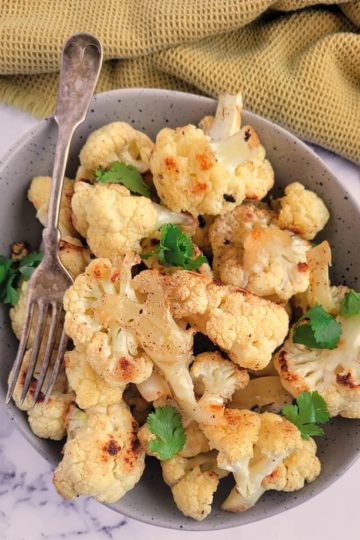 bowl of roasted cauliflower with chopped parsley, fork in the bowl