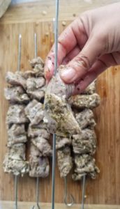 hand skewering pork souvlaki on metal skewers