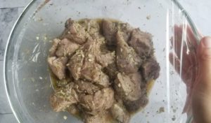 bowl of marinating pork pieces in a bowl covered with siran wrap