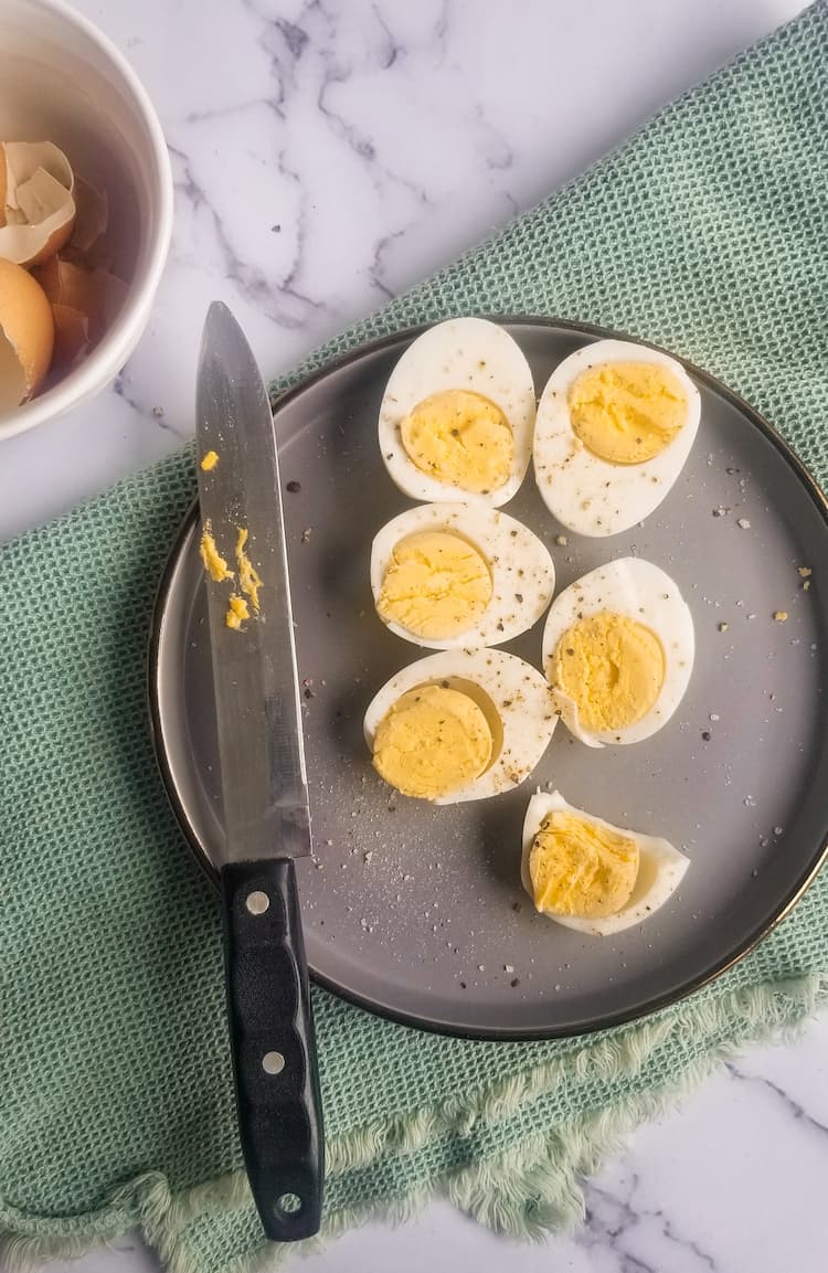 plate with halved hard boiled eggs next to a knife and bowl of shells
