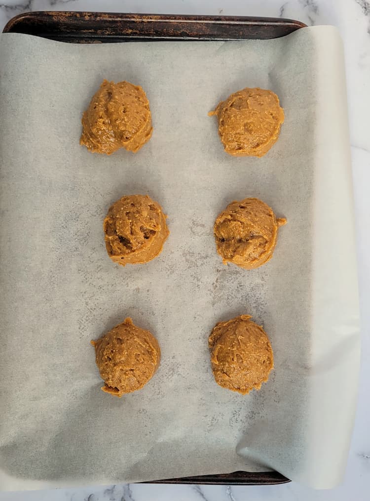 parchment lined baking sheet with 6 balls of peanut butter cookie batter